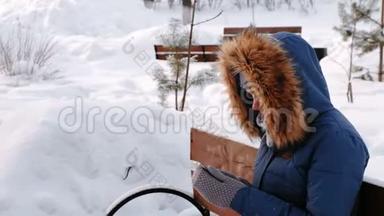 白天雪天，在冬天的城市<strong>公园里</strong>，女人<strong>坐在</strong>长椅上浏览手机